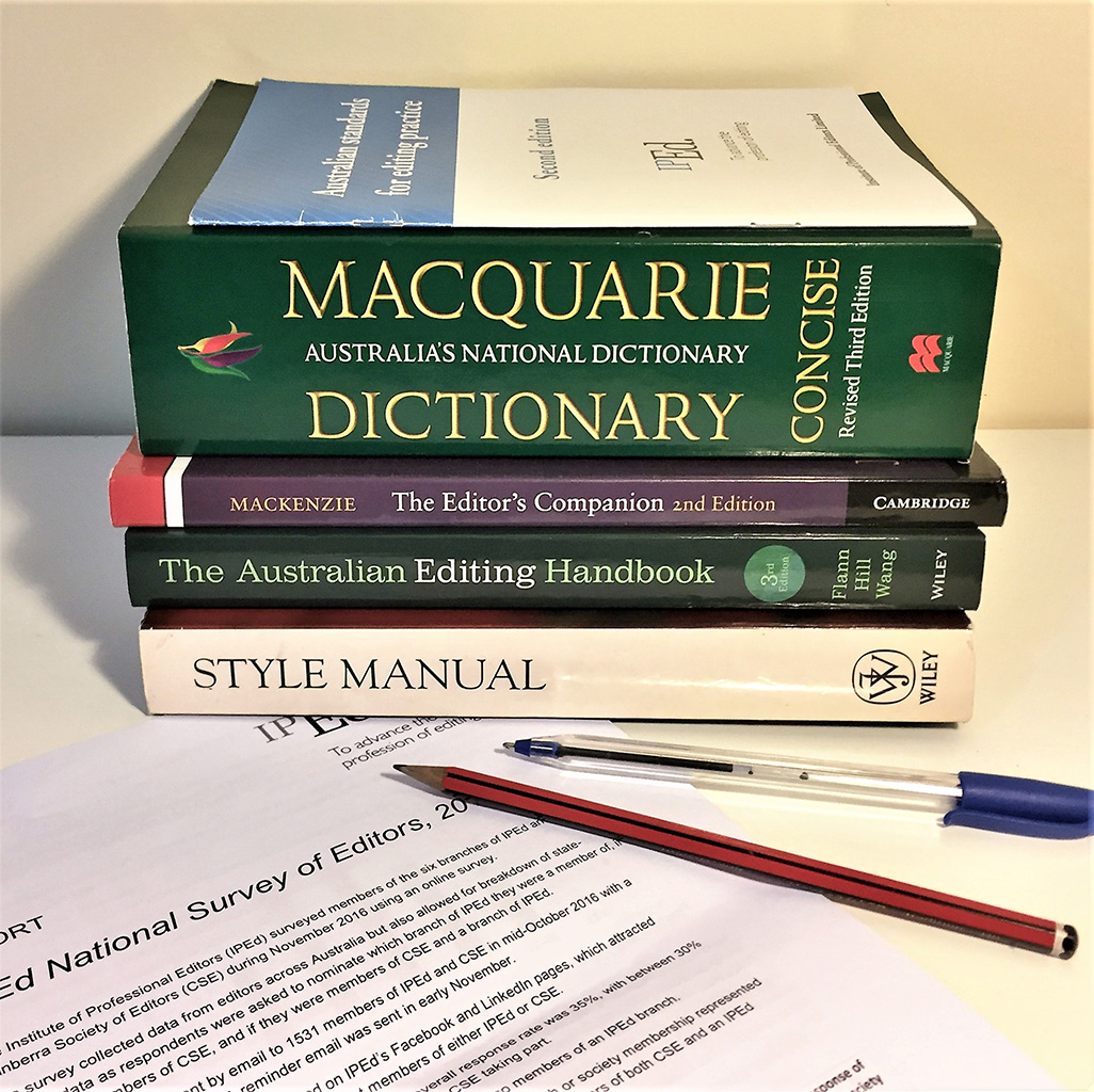 A pile of editorial resource books sit next to a pen and a paper document.