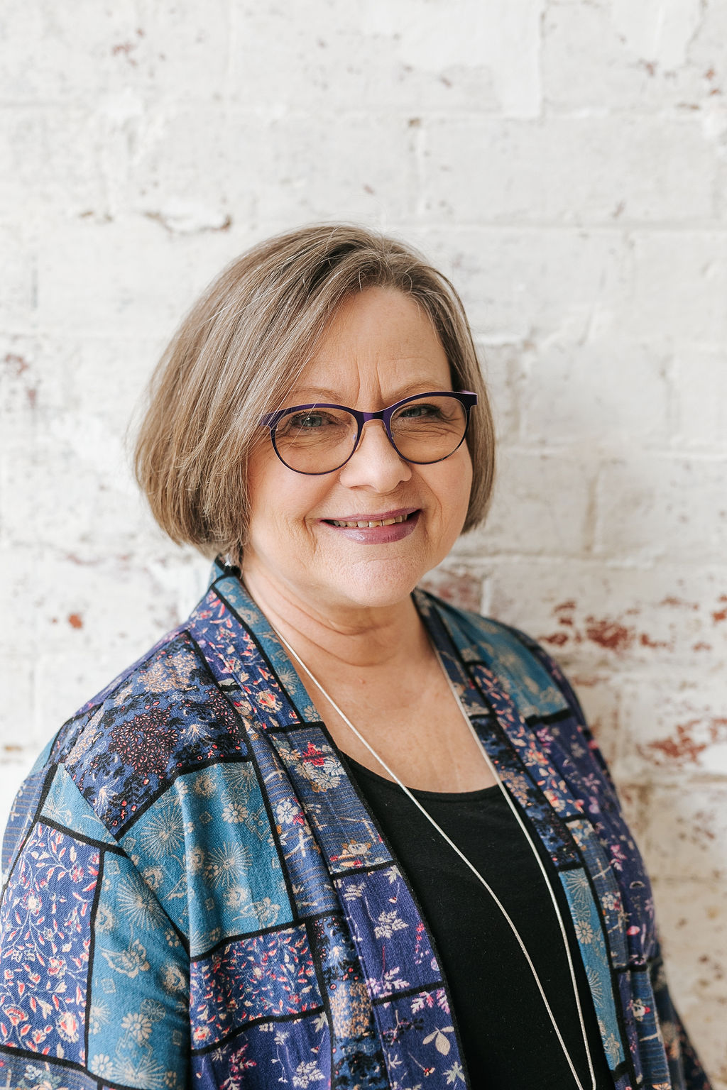 Photo shows lead editor Lee Ellwood, wearing glasses and a blue patchwork-style shirt over a black top.